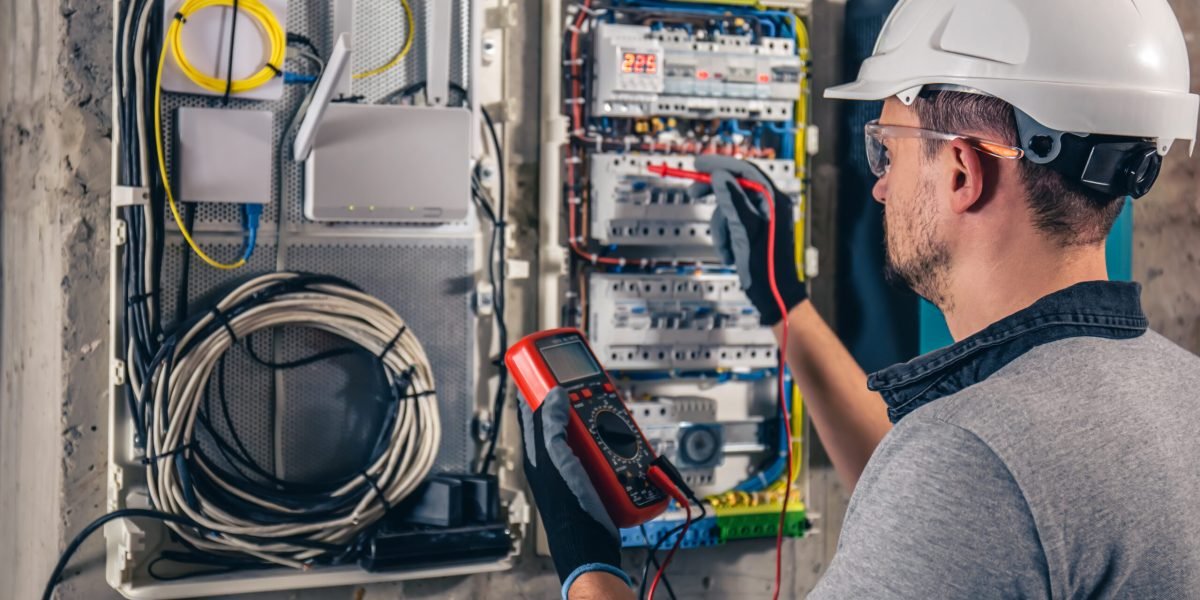 Man, an electrical technician working in a switchboard with fuses. Installation and connection of electrical equipment. Professional uses a tablet.