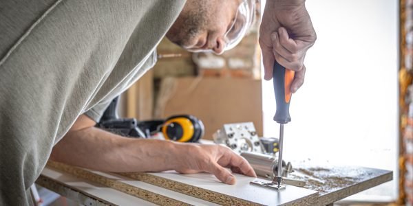 Screwing a self-tapping screw into a metal fastening hole on a wood strip using a screwdriver, the work of a carpenter.